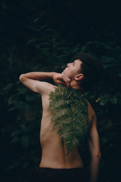 人与植物的图片-无上装的男人站着，用绿色的蕨类植物盖住他的背。