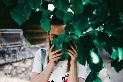 人与植物的图片-拿着树叶遮住脸的女人