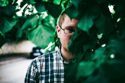 人与植物的图片-戴眼镜的男人站在绿叶后面