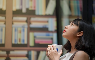 图书馆的图片-穿白衬衫的女人举着白色陶瓷杯子看着上面