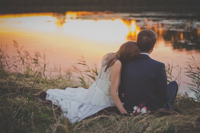从此幸福的图片-日落时分，一对新婚夫妇坐在水面前的绿草上。