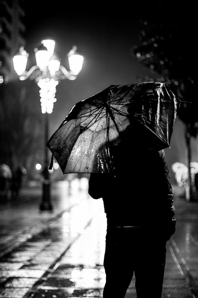 雨天的图片-柱旁撑伞人的灰度摄影